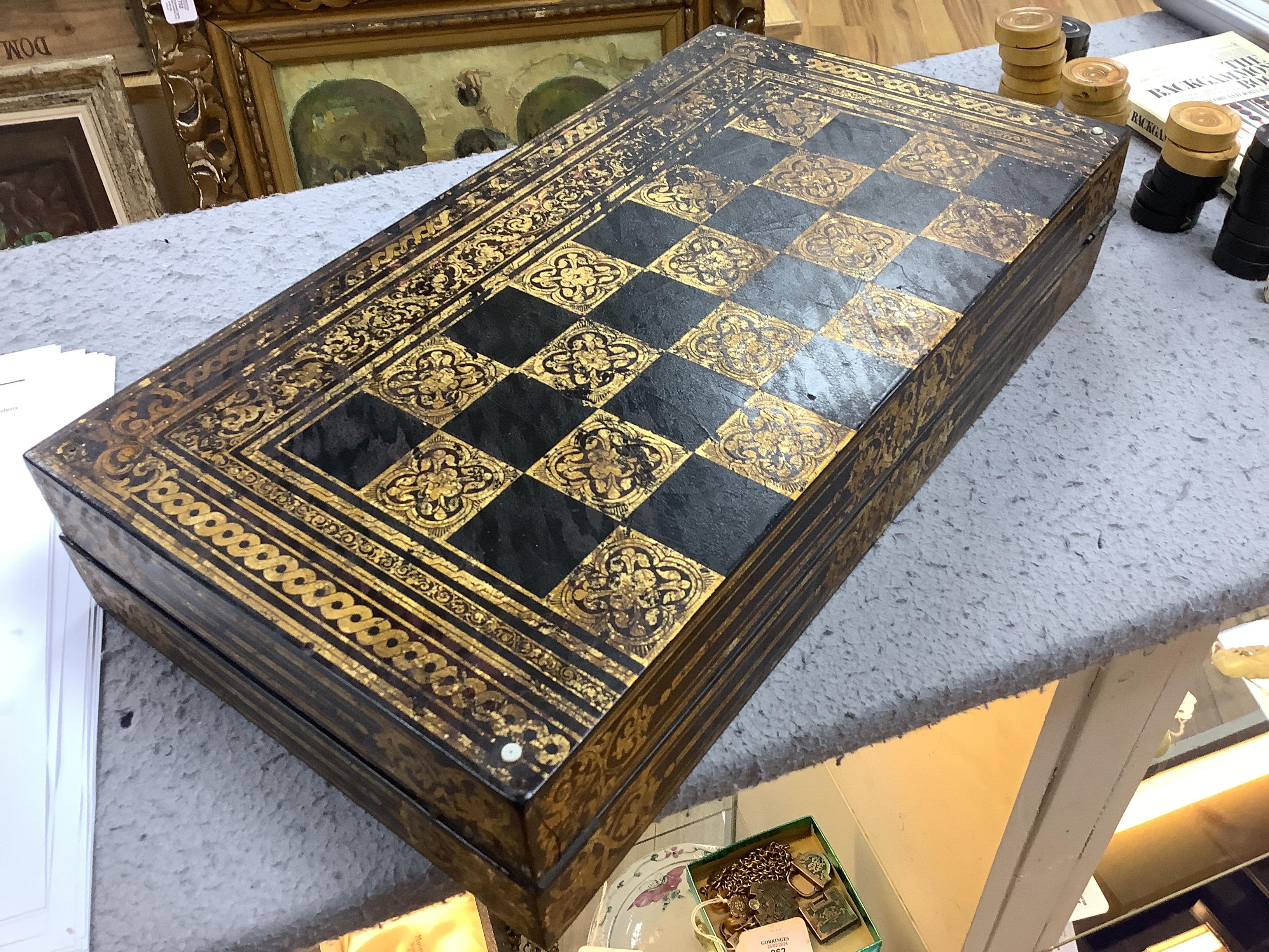 A 19th century papier maché folding games board for chess and backgammon, containing a wooden draughts set etc. with gilt decoration, 41 x 45cm unfolded